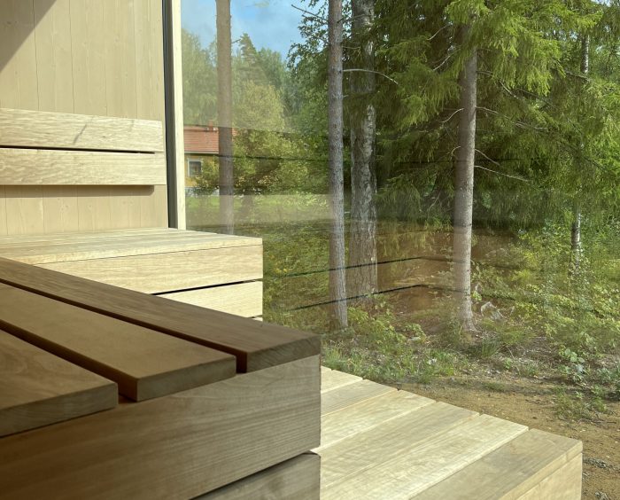 Saunan sisätilat, joissa on puisia penkkejä ja näkymä metsään ikkunan läpi.