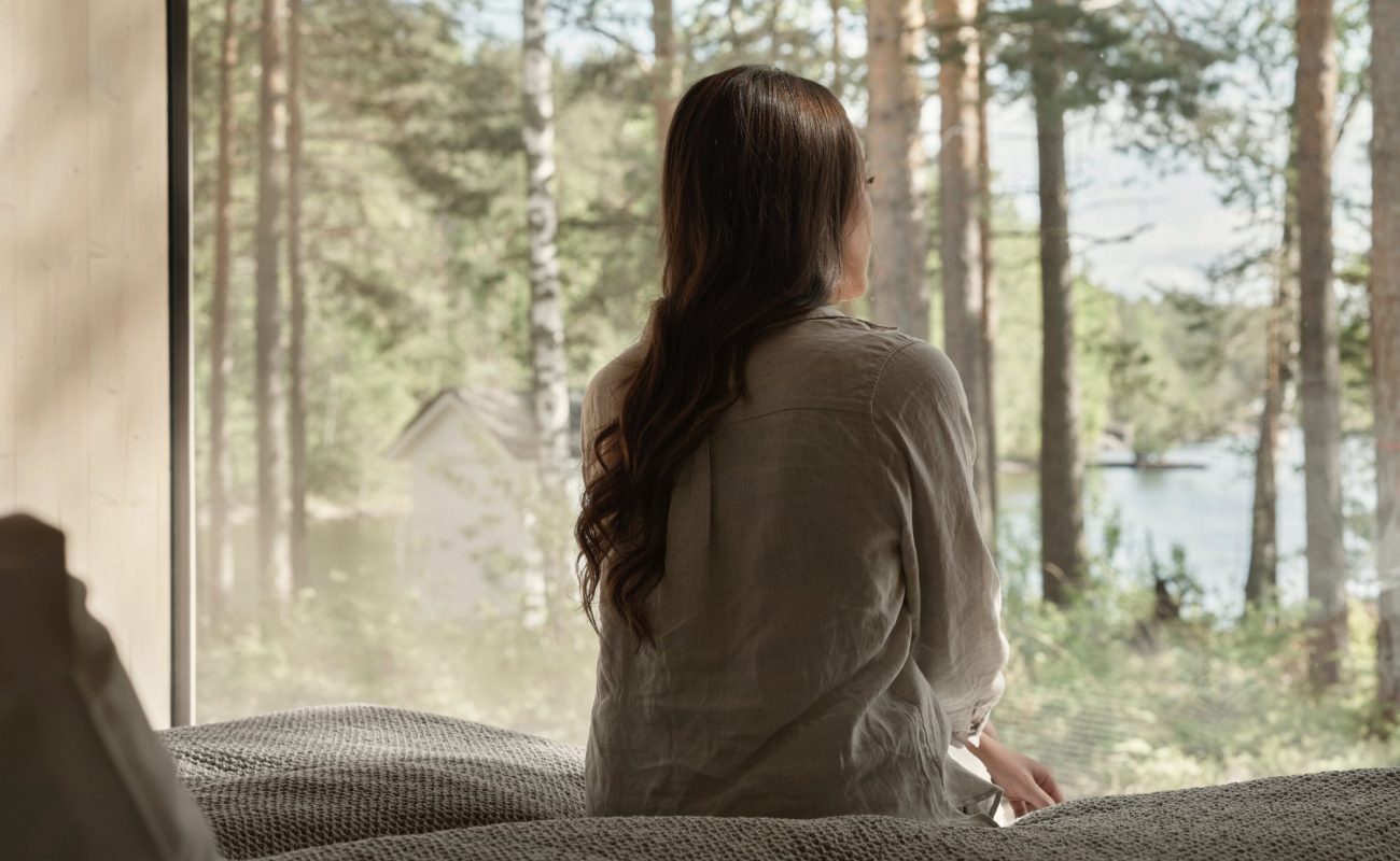 Eine Frau sitzt auf einem Bett und genießt den schönen Blick auf den Wald am See.