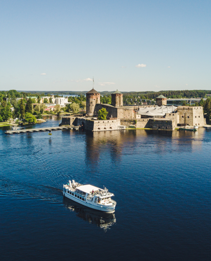 A beautiful landscape featuring a castle by the lakeshore with a boat sailing in the water.